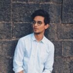 Stylish young man with eyeglasses posing against a brick wall outdoors.